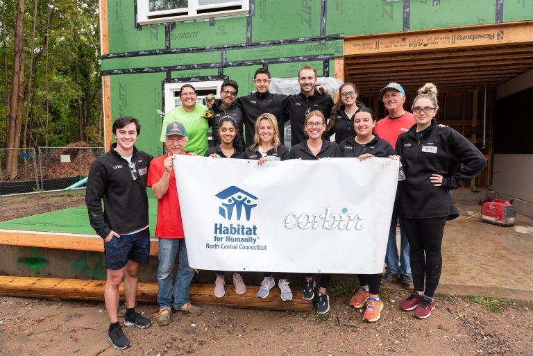 Love, Corbin team at the Habitat for Humanity build 2022: the team holding a banner with the Corbin and Habitat for Humanity logos
